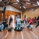 Grupo de artistas realizando una dinámica corporal en silla de ruedas y de pie.