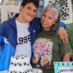 Artista con discapacidad junto a una emprendedora en su puesto.