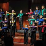 Niñas, niños y jóvenes realizan una interpretación coral con movimientos coordinados.
