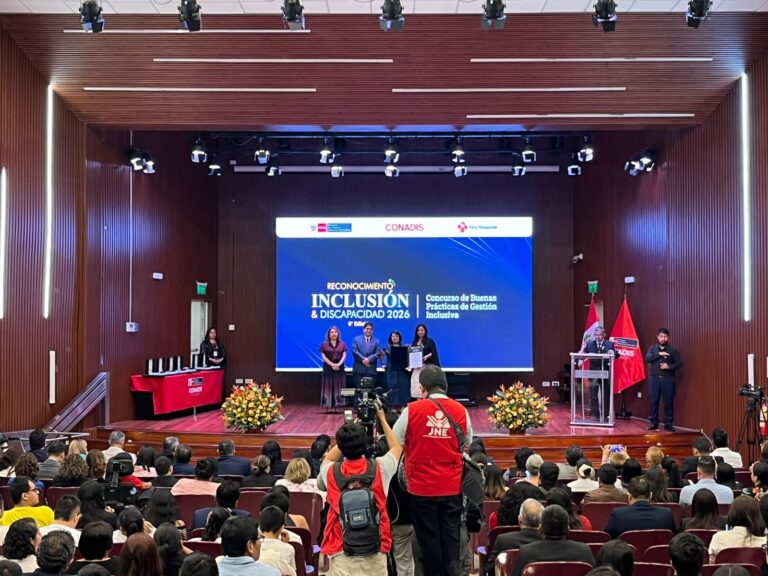La directora de CAPAZ Perú, Déborah Grandez Seminario, recibe un diploma de reconocimiento en el escenario durante la ceremonia del «Reconocimiento Inclusión & Discapacidad 2026» de CONADIS, frente a un auditorio lleno de gente.